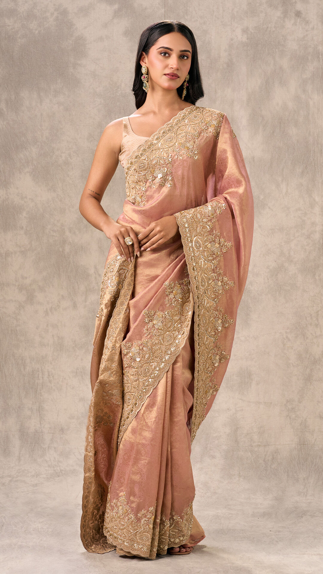 Woman modeling a subtle pink saree with heavy gold thread and sequin embroidery, demonstrating a regal styling tip.